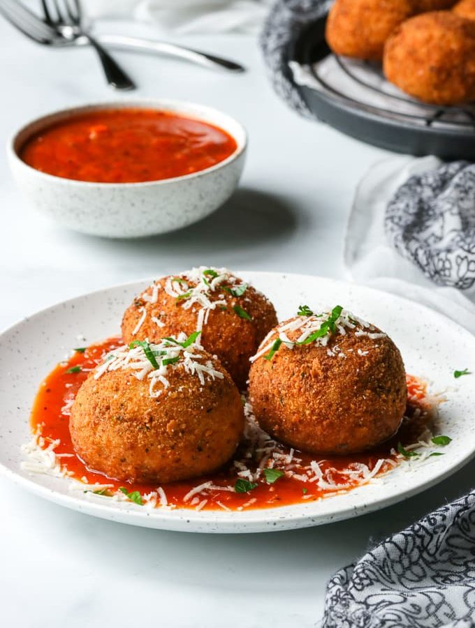 Three arancini on a white plate, served with a marinara sauce.