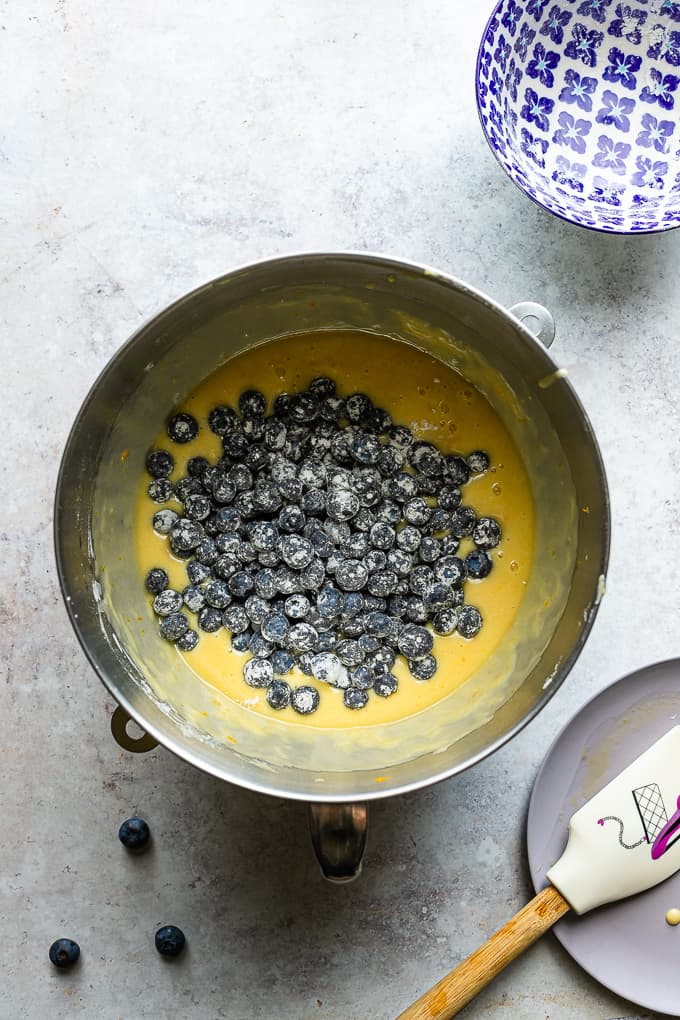 A metal mixing bowl with cake batter and topped with blueberries.