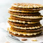 Anise and chocolate pizzelle cookies stacked up on a black wire rack.
