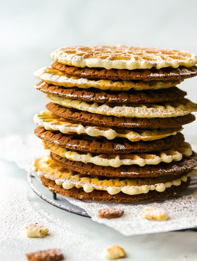 Anise and chocolate pizzelle cookies stacked up on a black wire rack.