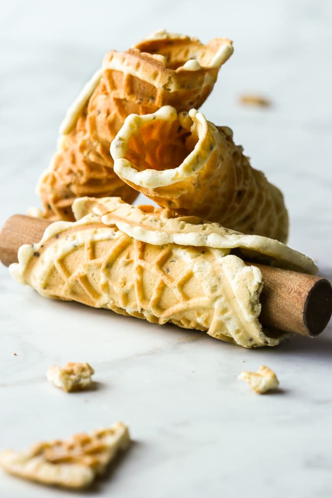 Three Pizzelle cookies shaped into cannoli with a wooden dowel.
