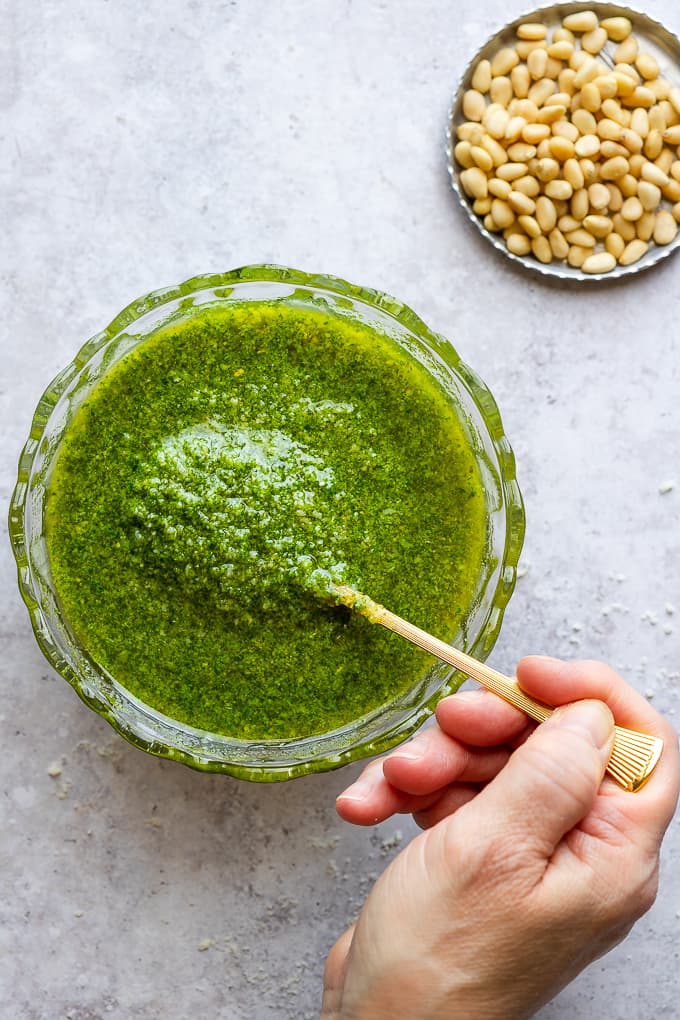 Stirring parmesan cheese with basil pesto in a small glass bowl.