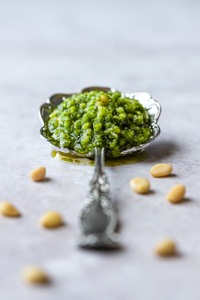 A silver tablespoon filled with basil pesto and pine nuts scattered around.
