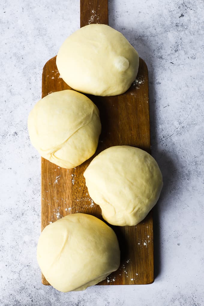 Four round shaped sweet bread dough on a brown wooden board.