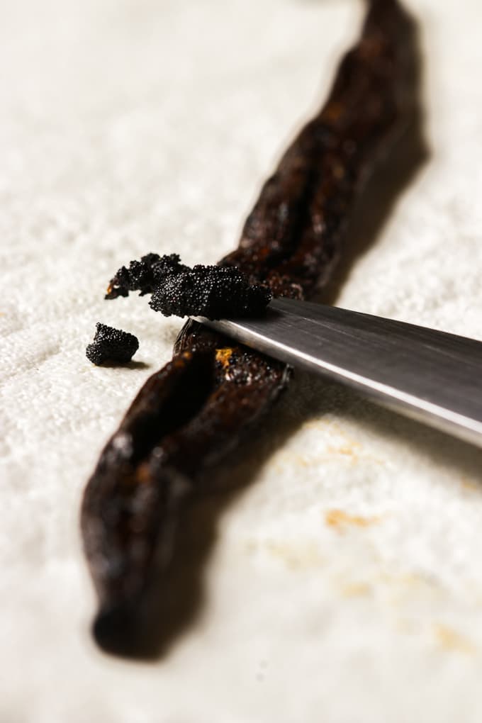 One vanilla bean sliced through while removing the seed with a silver knife.