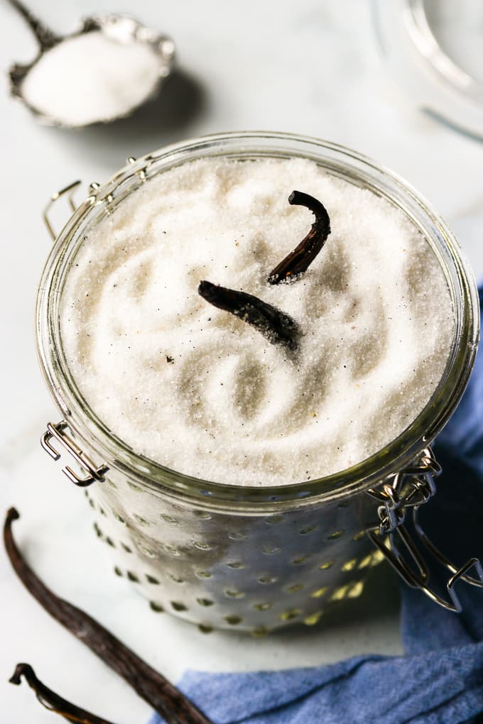 Homemade vanilla sugar in a glass jar with two whole vanilla beans inside.