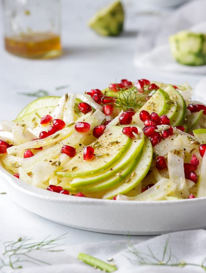 Green apple and fennel salad topped with pomegranate arils on a white plate.