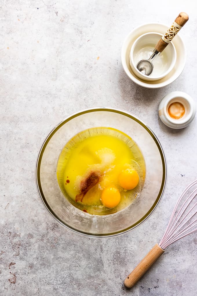 Eggs, sugar, oil and extracts in a glass bowl.