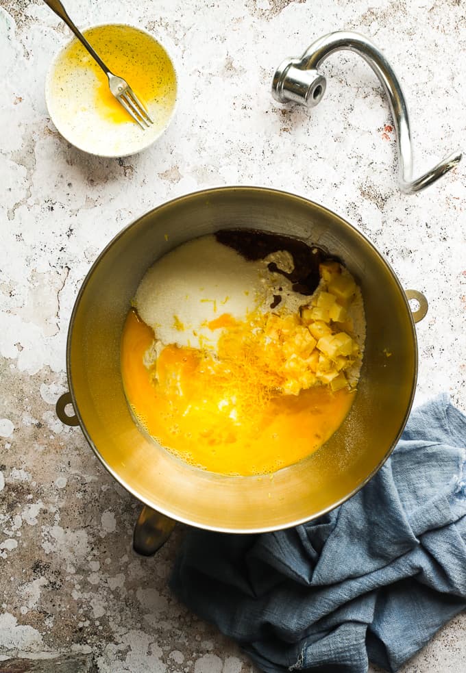 Mixing in eggs, sugar, lemon zest and vanilla extract in a grey mixing bowl.