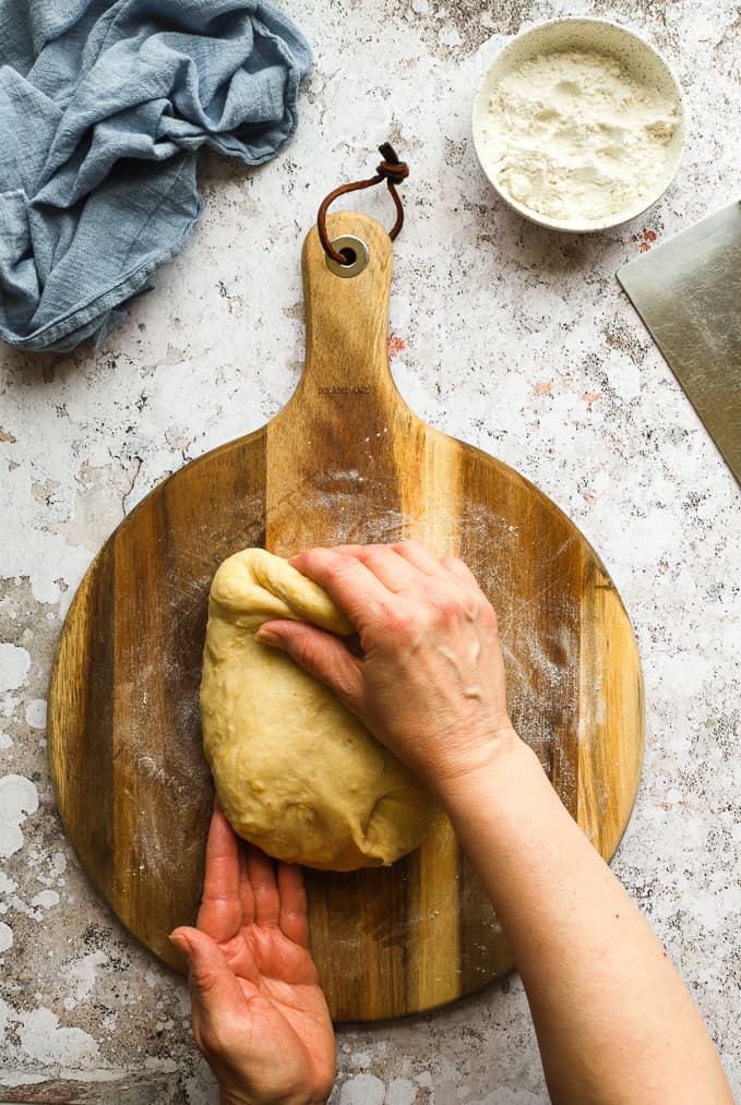 Kneading by hand the castagnole dough on a brown wooden board.
