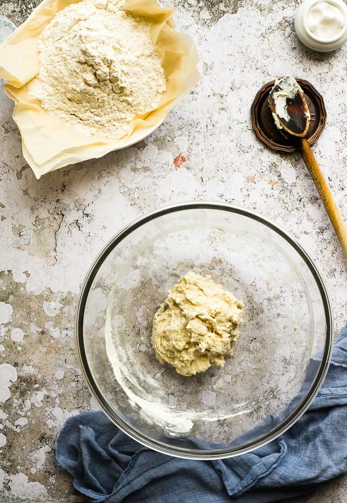 Flour and yeast mixture in a glass bowl with a wooden spoon in the background.