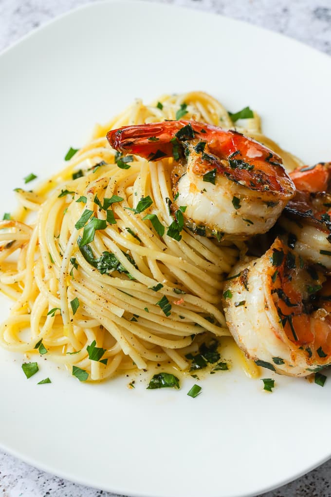 A serving of lemon spaghetti on a white plate topped with 3 lemon garlic shrimp.