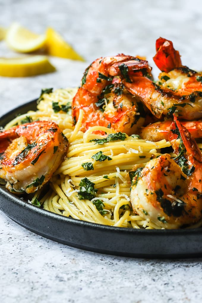 Pan seared shrimp topped over lemon pasta noodles on a black plate.