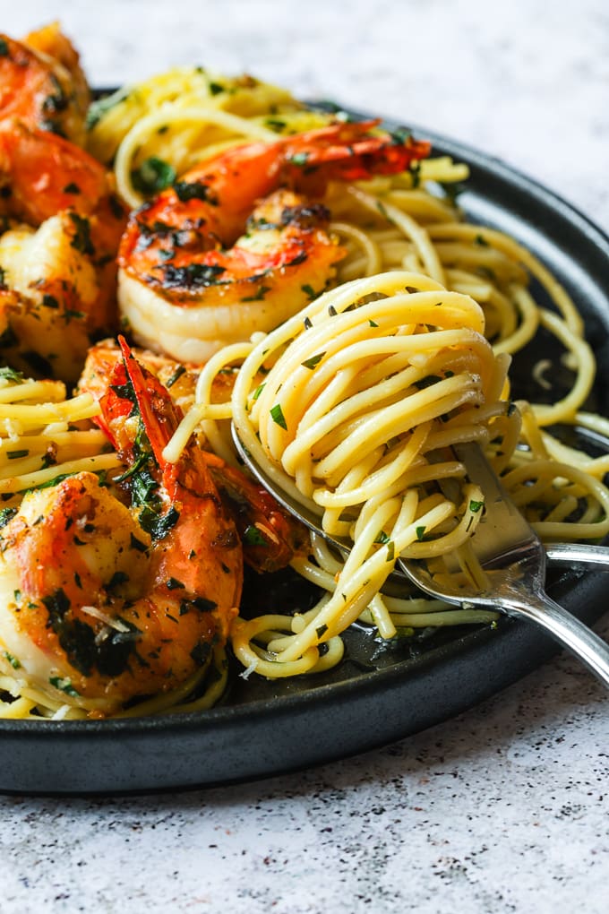 A black plate filled with lemon spaghetti and shrimp with a forkful of spaghetti twirled around the fork.
