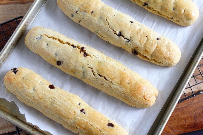 Four biscotti logs cooling on a parchment lined cookie tray.