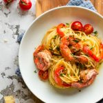 Pasta with shrimp and bell peppers in a white plate.