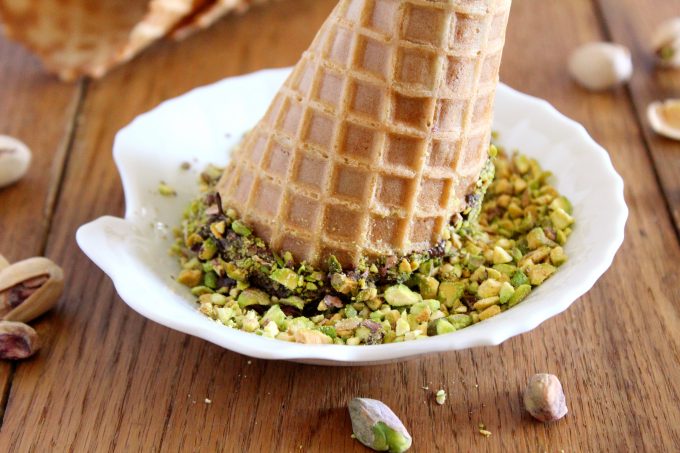 An ice-cream cone dipped in chocolate and chopped pistachios.
