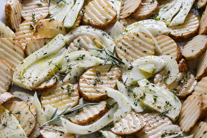 Slices of vegetables with spices on a baking tray.