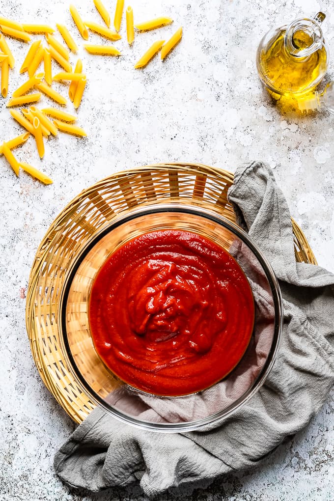 Tomato passata in a glass bowl with a grey napkin on the side.