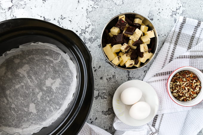 Slow cooker lined with parchment paper with a bowl of chocolate and butter.
