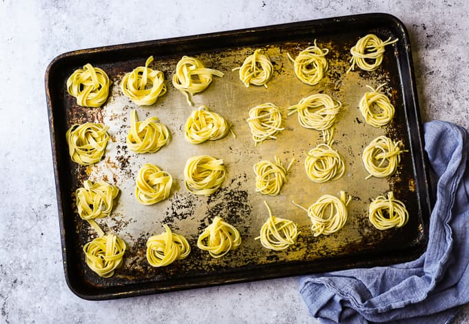 Fresh Capellini and Tagliatelle pasta shaped into nests on a steel baking tray.