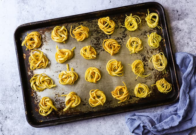 Deep fried swirled tagliatelle and capellini pasta on a steel baking tray.