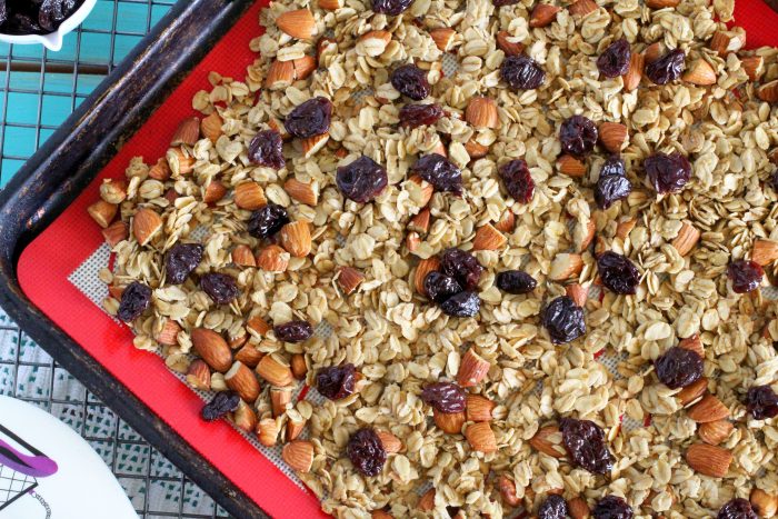 Freshly made granola with almonds, rolled oats and dried cherries on metal cookie sheet.