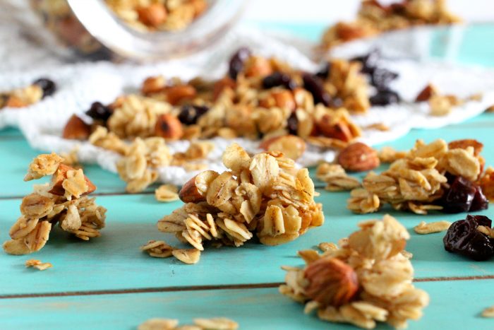 Clusters of cherry granola on a white napkin with a glass jar filled with granola in the background.