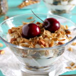 Two individual servings of a yogurt parfait in stemmed glasses topped with cherry granola.