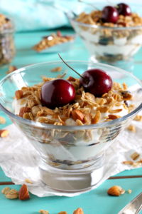Two individual servings of a yogurt parfait in stemmed glasses topped with cherry granola.
