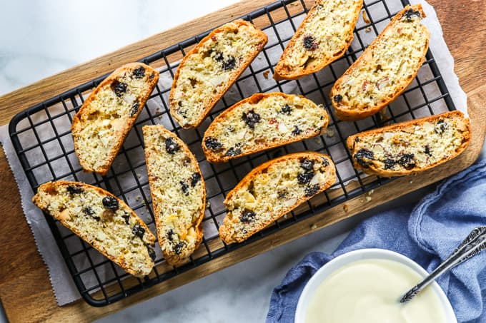Sliced biscotti with blueberries and white chocolate on a cooling rack placed over a wooden board.