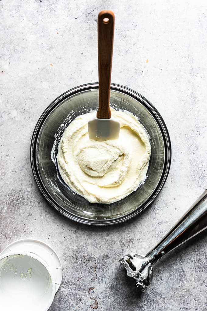 A glass bowl with whipped ricotta and a spatula in the bowl.