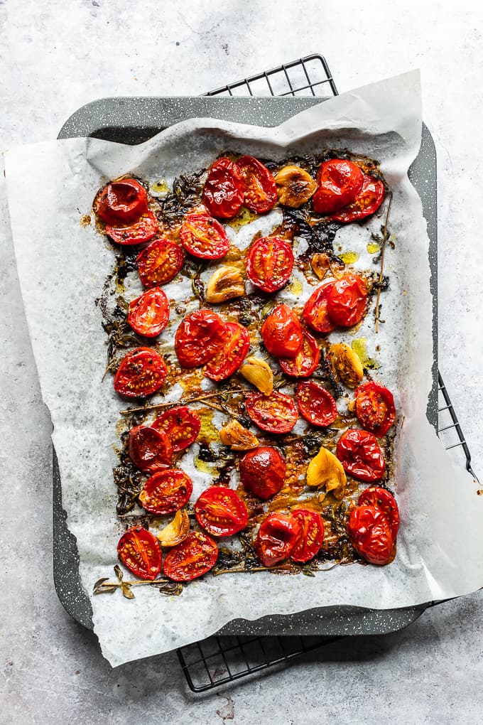 Oven roasted cherry tomatoes on a grey baking sheet lined with parchment paper.