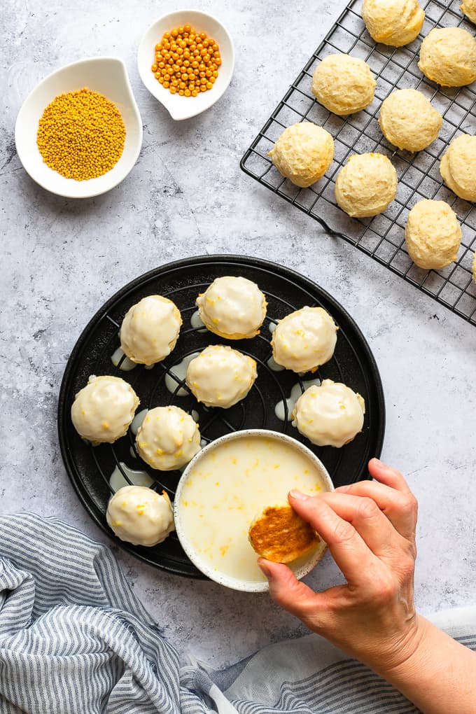 Dipping ricotta cookies in a lemon glaze and set over a wire rack and black plate.