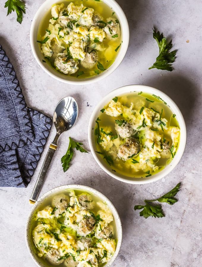 Three white bowls filled with stracciatella soup and mini meatballs.