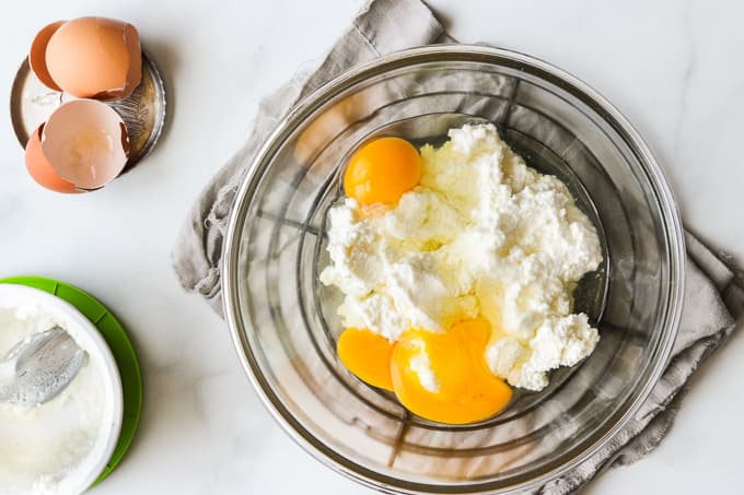 Beating eggs and ricotta together in a glass bowl.