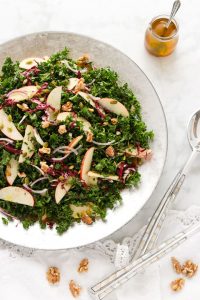 Loaded kale salad with apples and walnuts on a silver tray.