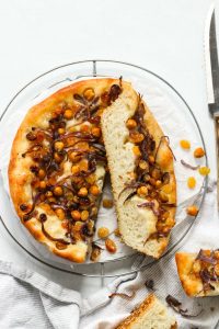 Baked focaccia topped with chickpeas, red onion and raisins.
