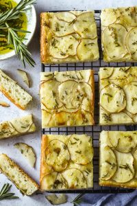 Six slices of potato and rosemary focaccia on a black cooling rack.