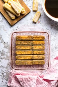 Coffee soaked ladyfingers lined up in a pink glass square pan.