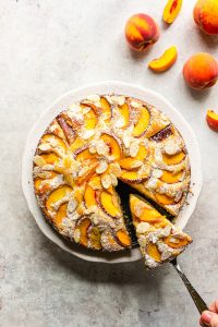 Fresh peach and almond cake with one slice cut off, on a white cake stand.