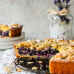 Blueberry and almond crumble cake with blueberries and almonds, with a slice cut off.