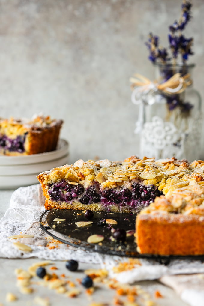 Blueberry and almond crumble cake with blueberries and almonds, with a slice cut off.
