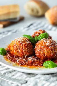 Three meatballs served with tomato sauce on a white plate.